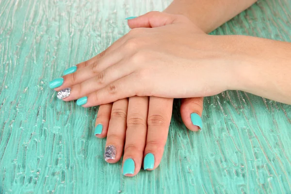 Mooie vrouw handen met blauwe manicure, op een achtergrond met kleur — Stockfoto