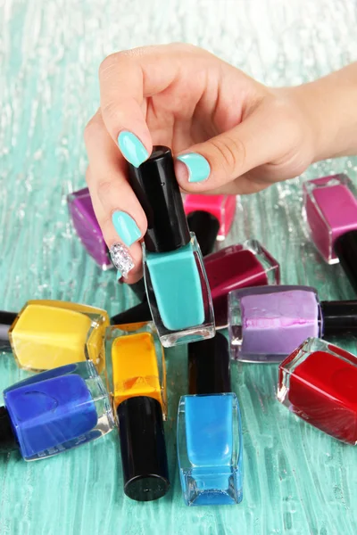 Beautiful woman hands with blue manicure and several bottles with nail polish, on color background — Stock Photo, Image