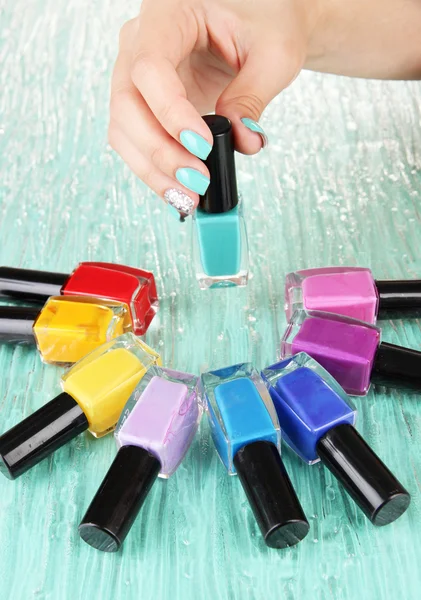 Beautiful woman hands with blue manicure and several bottles with nail polish, on color background — Stock Photo, Image