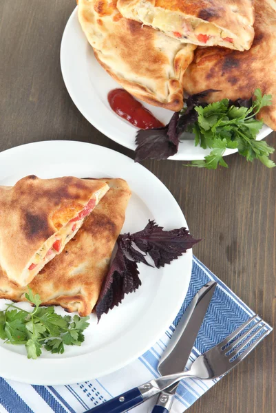 Pizza calzone on plates on napkin on wooden table — Stock Photo, Image