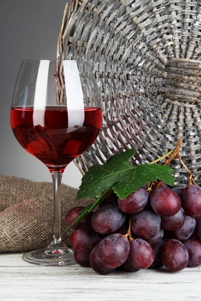 Zralé vynikající hrozny se sklenicí vína na stole na šedém pozadí — Stock fotografie