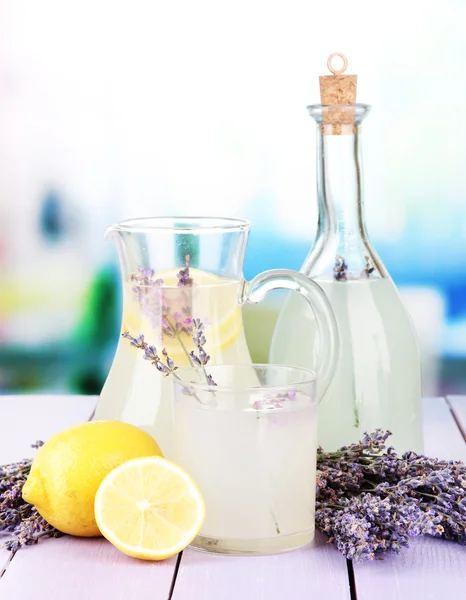 Lavendellimonade in Glasflasche und Krug, auf violettem Holztisch, auf hellem Hintergrund — Stockfoto