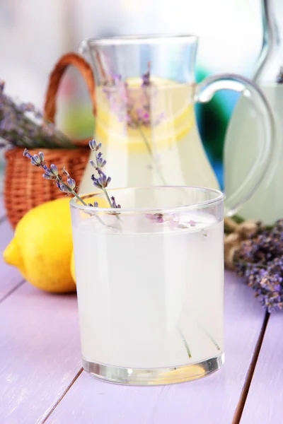 Lemoniada lawendy w szklanej butelce i dzbanek na fioletowe drewniany stół, na jasnym tle — Zdjęcie stockowe