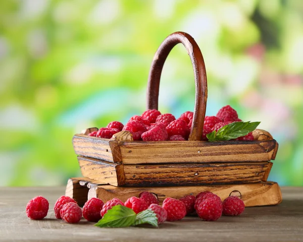 Frambuesas dulces maduras en cesta sobre mesa de madera, sobre fondo verde —  Fotos de Stock