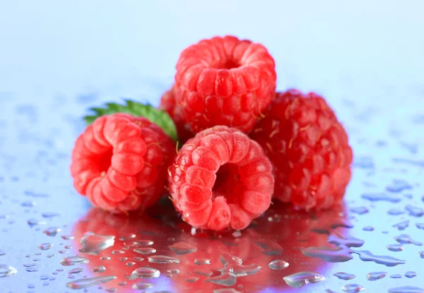 Ripe sweet raspberries with drops, on blue background — Stock Photo, Image