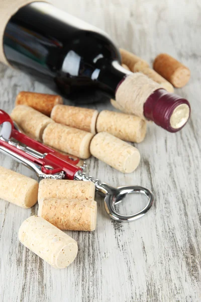 Corkscrew with wine corks and bottle of wine on wooden table close-up — Stock Photo, Image