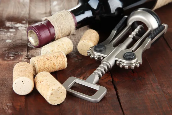 Corkscrew with wine corks and bottle of wine on wooden table close-up — Stock Photo, Image