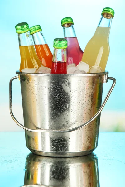 Botellas con sabrosas bebidas en cubo con cubitos de hielo, en un fondo brillante —  Fotos de Stock