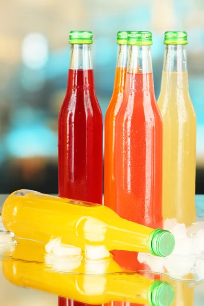 Bottles with tasty drinks with ice cubes, on bright background — Stock Photo, Image