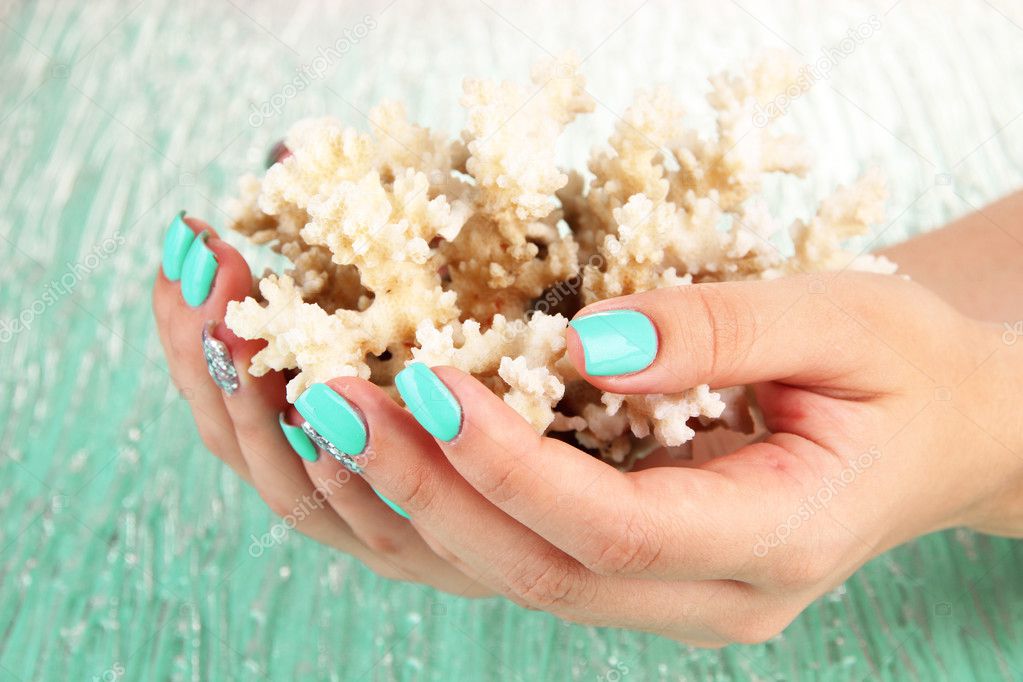 Beautiful woman hands with blue manicure holding coral, on color background