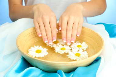 woman hands with wooden bowl of water with flowers, on blue background clipart