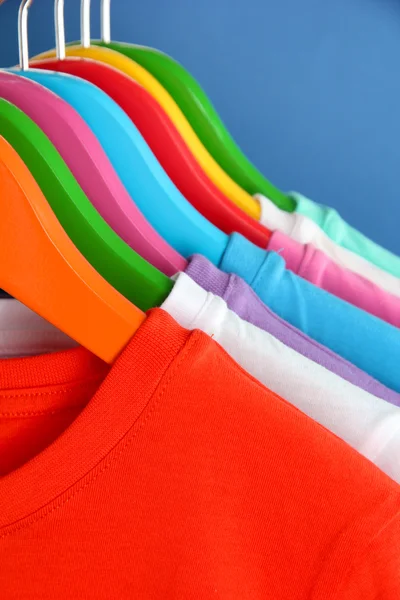 Verschillende shirts op kleurrijke hangers op blauwe achtergrond — Stockfoto