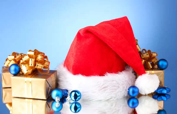 Bonito chapéu de Natal, presentes e bolas de Natal no fundo azul — Fotografia de Stock