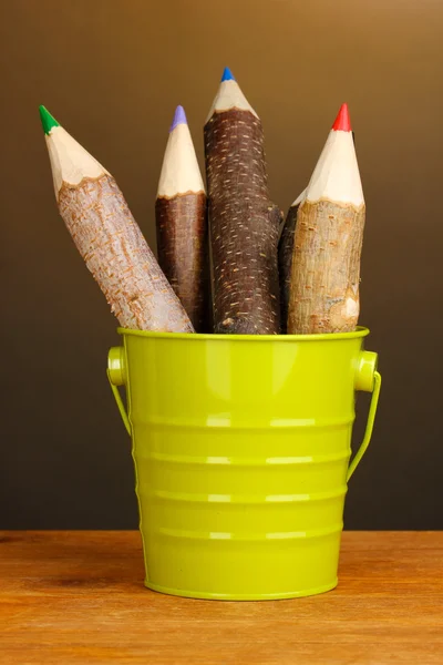 Цветные деревянные карандаши в зеленом ведре на деревянном столе на коричневом фоне — стоковое фото