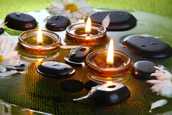 Piedras de spa con flores y velas en agua en el plato —  Fotos de Stock