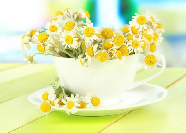 Bouquet of chamomile flowers in cup, on bright background — Stock Photo, Image