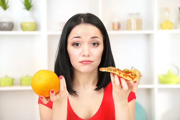 Mooi meisje selecteert pizza of dieet op keuken achtergrond — Stockfoto