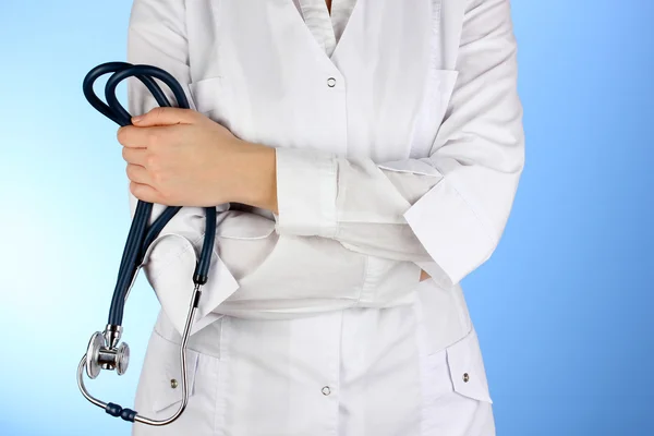 Médecin avec stéthoscope dans les mains sur fond bleu — Photo