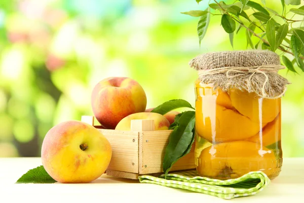 Jar of canned peaches and fresh peaches on wooden table, outside