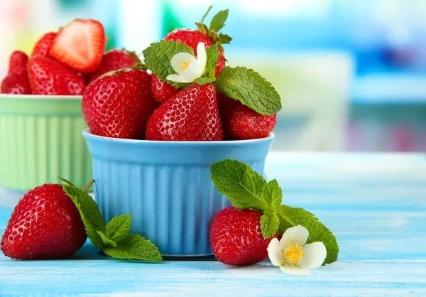 Rijpe zoete aardbeien in kommen op blauwe houten tafel — Stockfoto