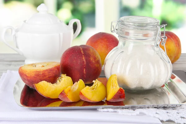Персики с сахаром на металлическом подносе на салфетке на столе на оконном фоне — стоковое фото