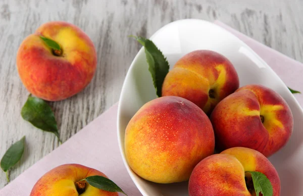 Peaches in plate on napkin on wooden table — Stock Photo, Image