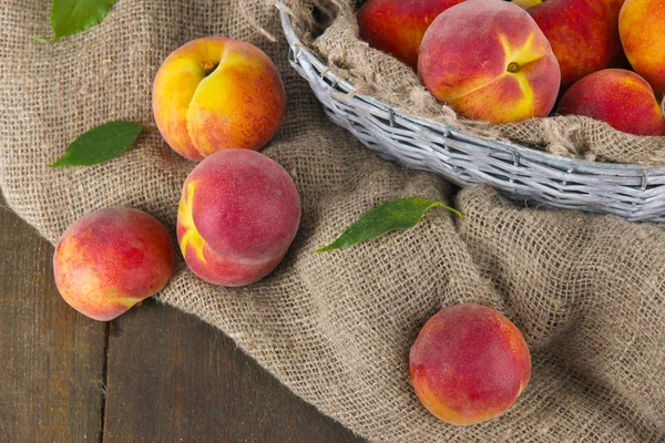 Peaches in basket on sackcloth on wooden table — Stock Photo, Image