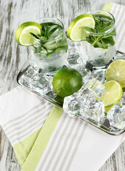 Glasses of cocktail with ice on metal tray on napkin on wooden table — Stock Photo, Image