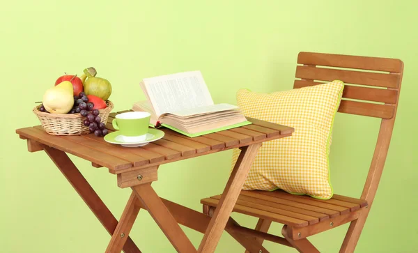 Table en bois avec fruits, livre et tasse sur fond vert — Photo