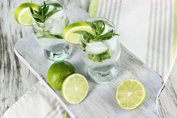 Glasses of cocktail with ice on board on napkin on wooden table — Stock Photo, Image