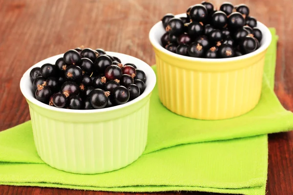 Fresh black currant in bowls on napkin on wooden background — Stock Photo, Image
