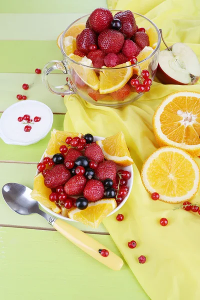 Ensalada de frutas útil en taza de vidrio y tazón en mesa de madera de primer plano — Foto de Stock