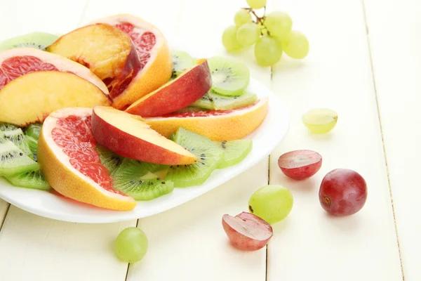 Assortment of sliced fruits on plate, on white wooden table — Stock Photo, Image