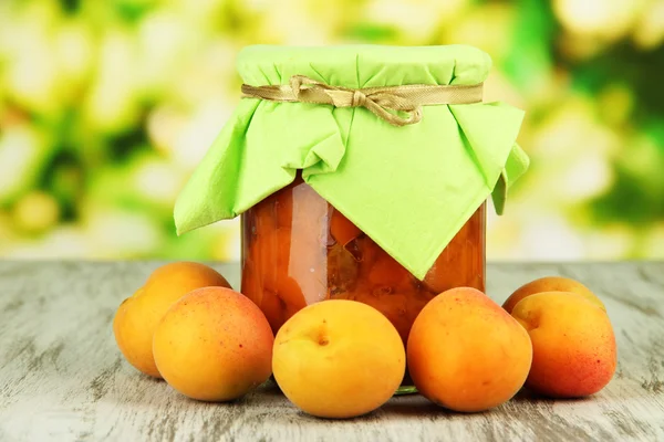 Marmellata di albicocche in vaso di vetro e albicocche fresche, su tavolo di legno, su sfondo brillante — Foto Stock