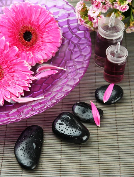 Gerbera flowers on water and spa stones on bamboo mat — Stock Photo, Image