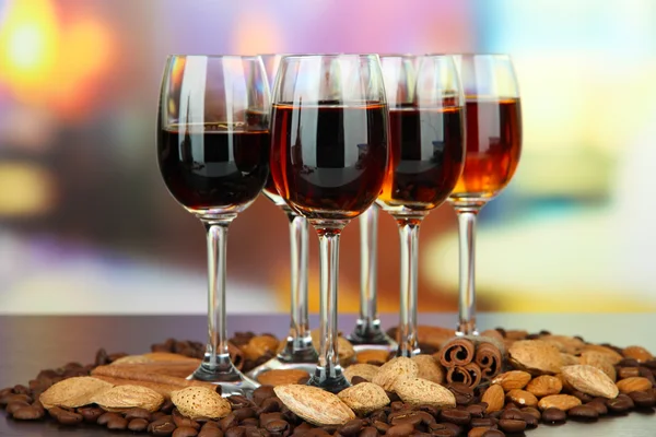 Glasses of liquors with almonds and coffee grains, on bright background — Stock Photo, Image