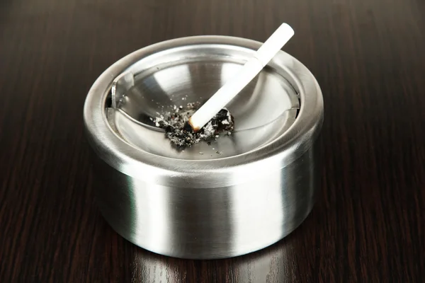 Metal ashtray and cigarette on wooden table — Stock Photo, Image