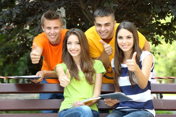 Happy group of young students sitting in park Stock Image
