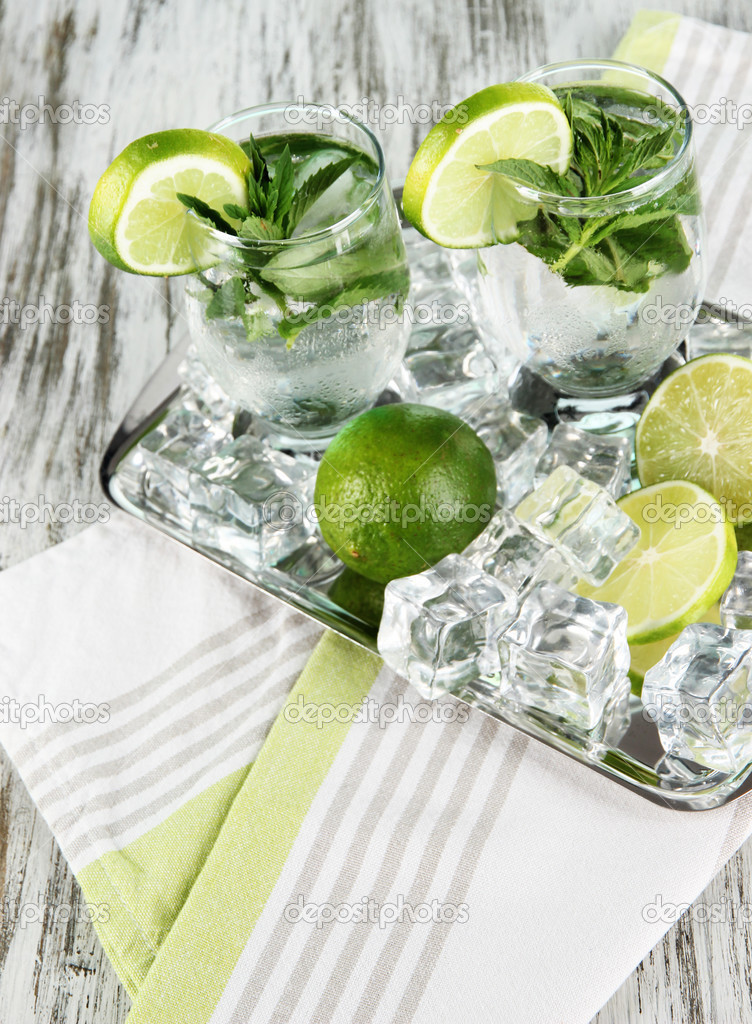 Glasses of cocktail with ice on metal tray on napkin on wooden table