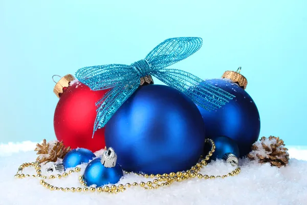 Mooie blauw en rode kerstballen en kegels op sneeuw op blauwe achtergrond — Stockfoto