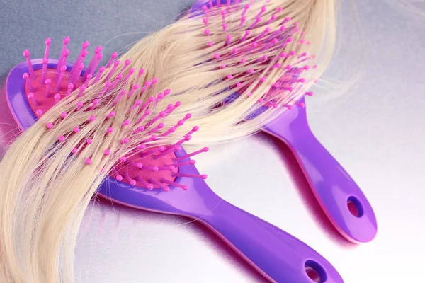 Blond curls brushing two combs on metalic background — Stock Photo, Image
