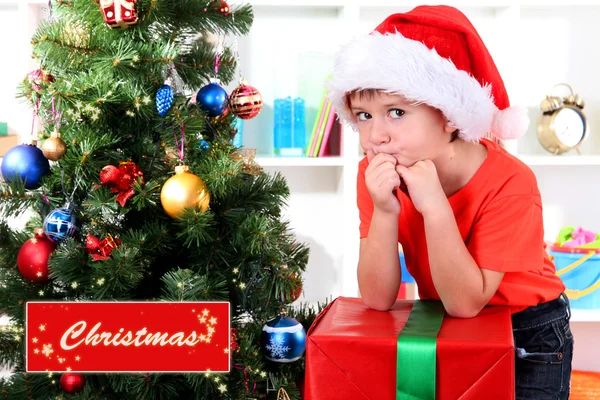 Enfant en chapeau de Père Noël près de l'arbre de Noël avec un grand cadeau — Photo