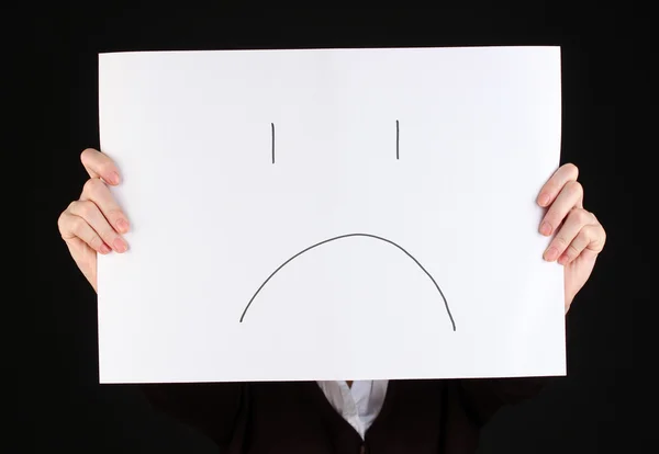 Woman holding paper with sad emoticon, isolated on black — Stock Photo, Image