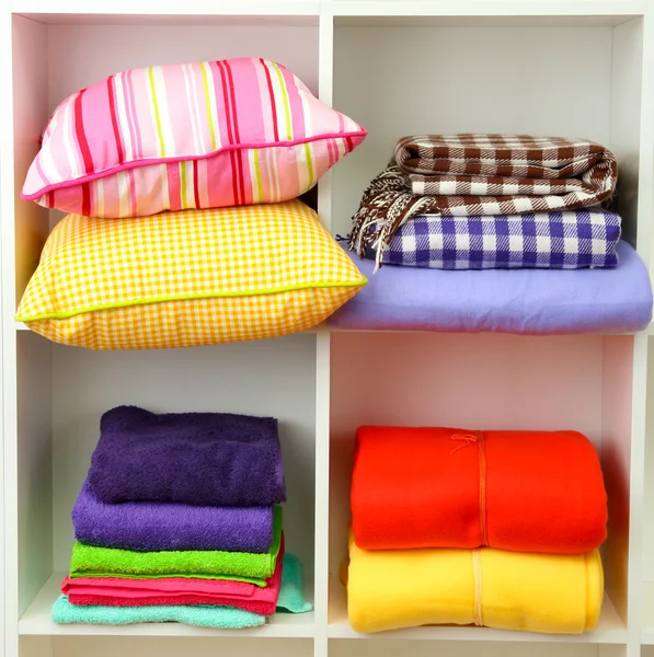 Bright pillows, towels and plaids on shelves, isolated on white — Stock Photo, Image