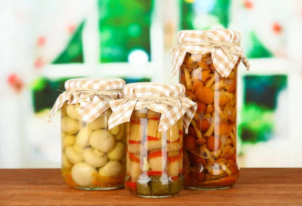 Delicious marinated mushrooms in glass jars, on wooden table on bright background — Stock Photo, Image