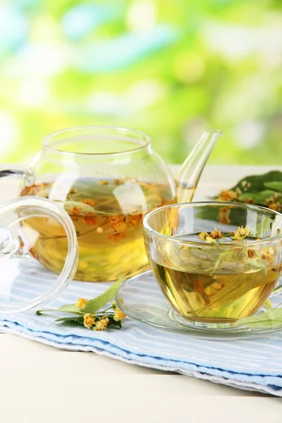 Kettle and cup of tea with linden on napkin on wooden table on nature background — Stock Photo, Image