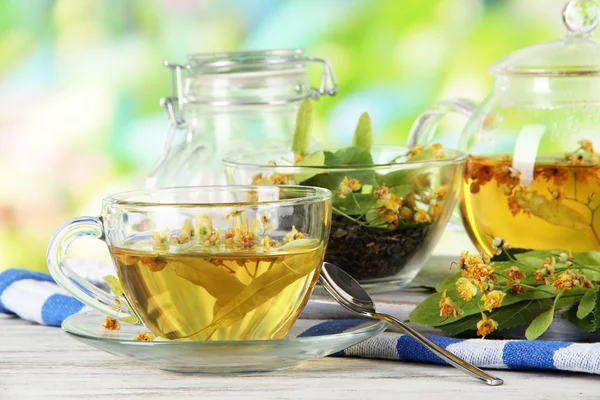 Konvice a šálek čaje s linden na dřevěný stůl na pozadí přírody — Stock fotografie