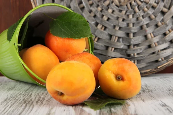 Abricots dans un seau sur une table en bois près des dessous de verre en osier — Photo