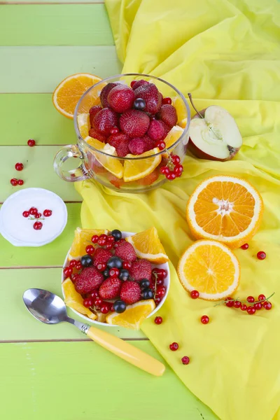 Ensalada de frutas útil en taza de vidrio y tazón en mesa de madera de primer plano — Foto de Stock
