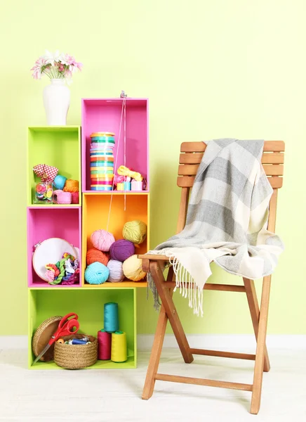 Colorful shelves of different colors with utensils near chair with plaid on wall background — Stock Photo, Image